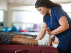 A lady physiotherapist giving therapy session to leg injured patient