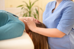 Female physiotherapist or a chiropractor adjusting patients neck. Physiotherapy, rehabilitation concept. Side view cropped shot.