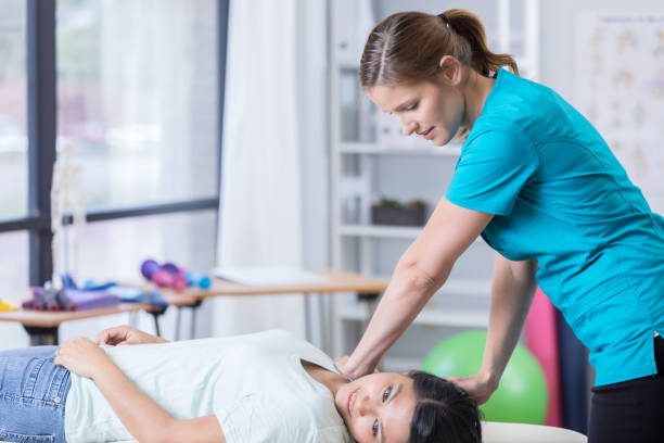 Mid adult Caucasian chiropractor works on mid adult Asian woman. The chiropractor is working on the woman's shoulder.