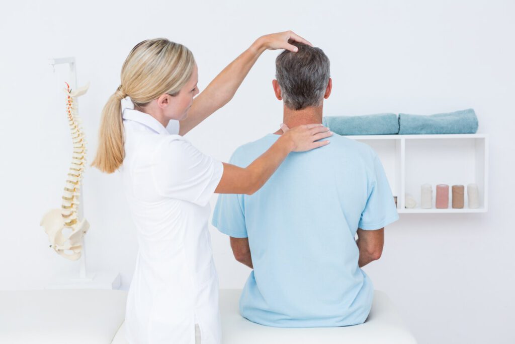 A female physical therapist is performing a neck adjustment on a male patient during spine physical therapy.