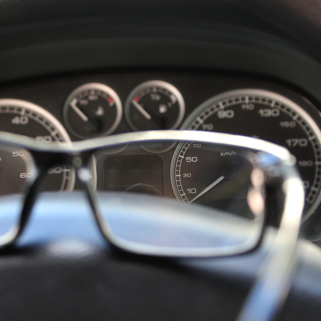 Lens of glasses focusing sharply on the speedometer dial while the rest of the car dashboard remains defocused, indicating a vision test during a DOT physical.