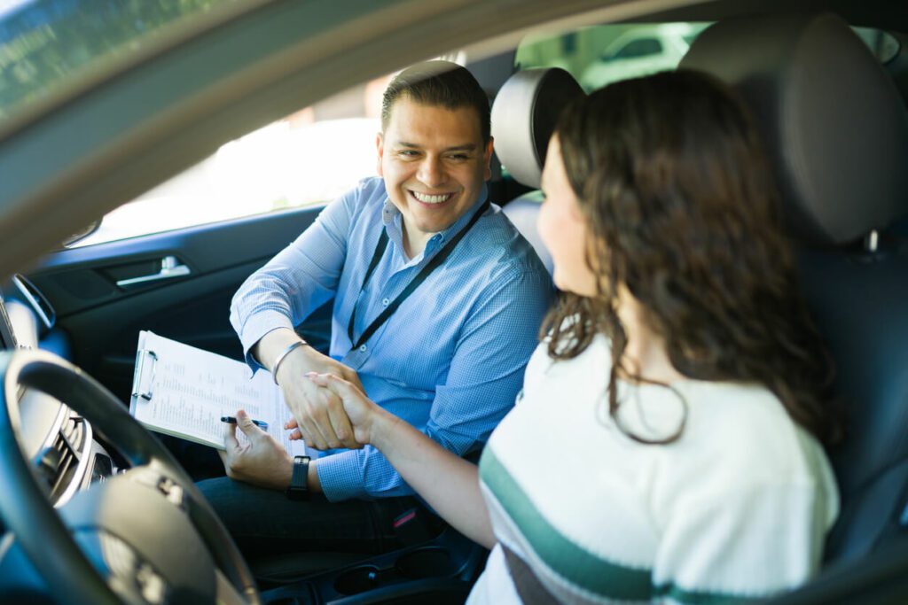Happy driving instructor shaking hands with his student after passing the driving test inside a car, after DOT physical.